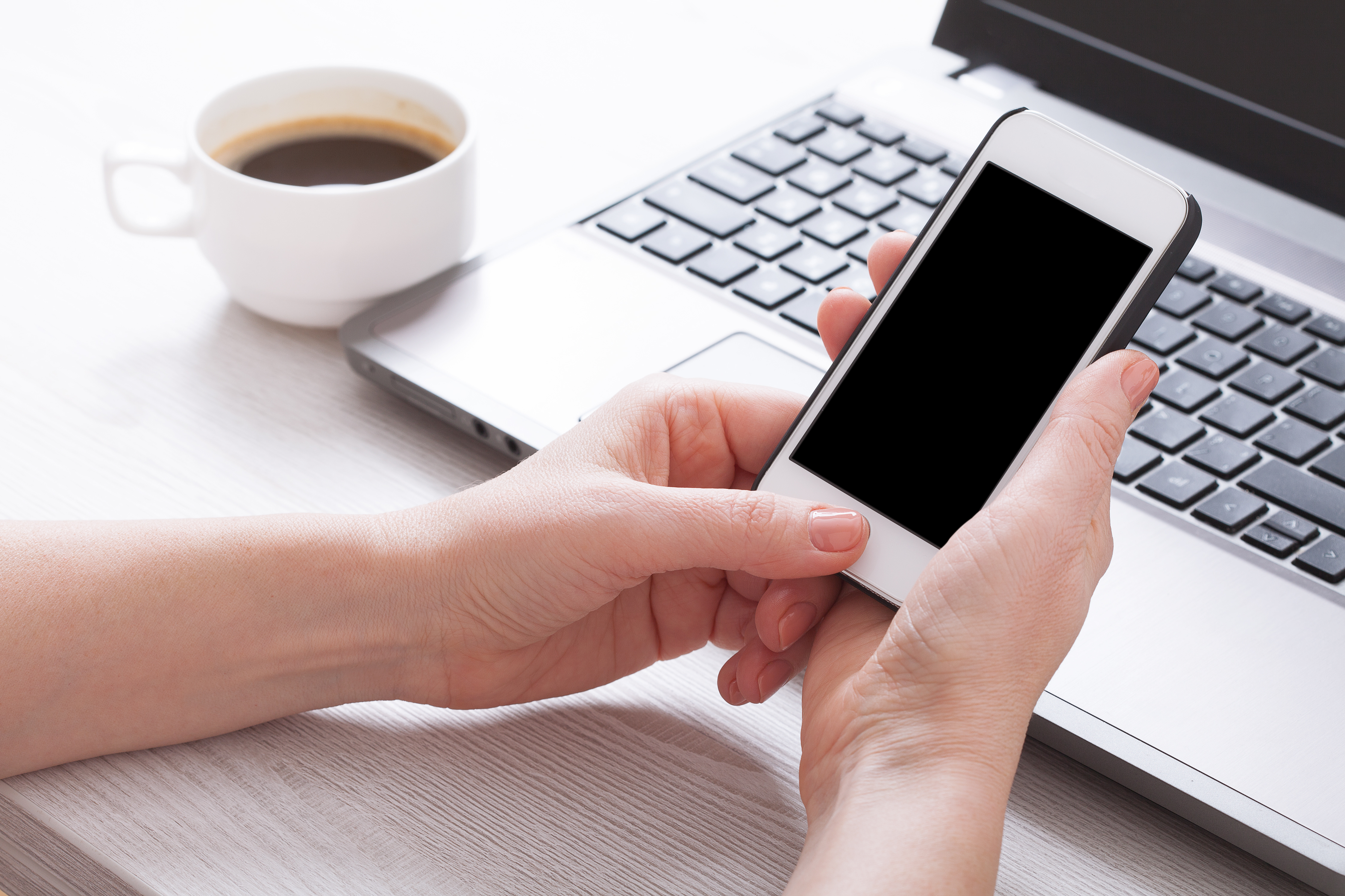 A woman holds smartphone white phone in the workplace in the room. Woman using a mobile phone for work.